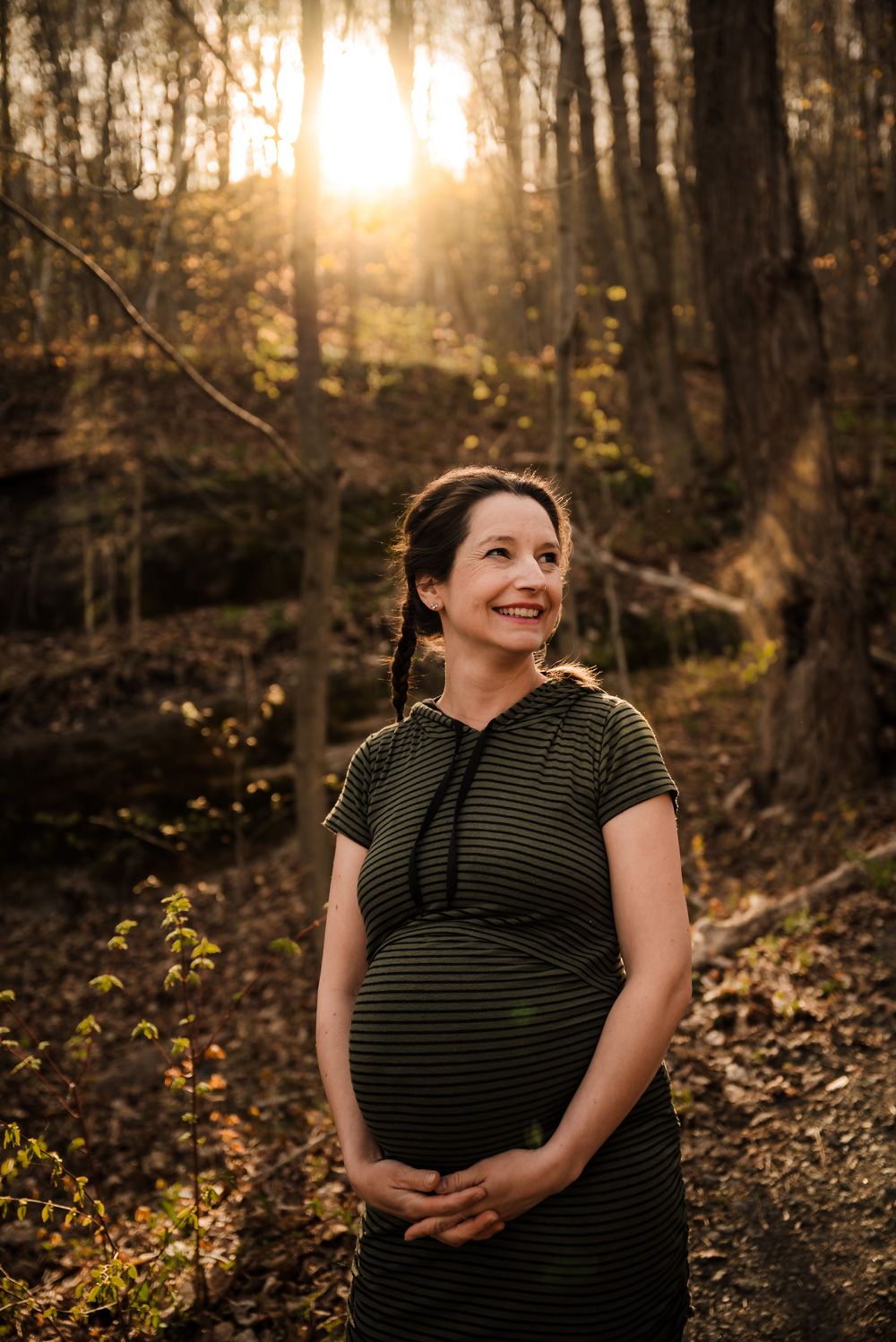 Maternity portrait in striped dress with sunlit forest background.