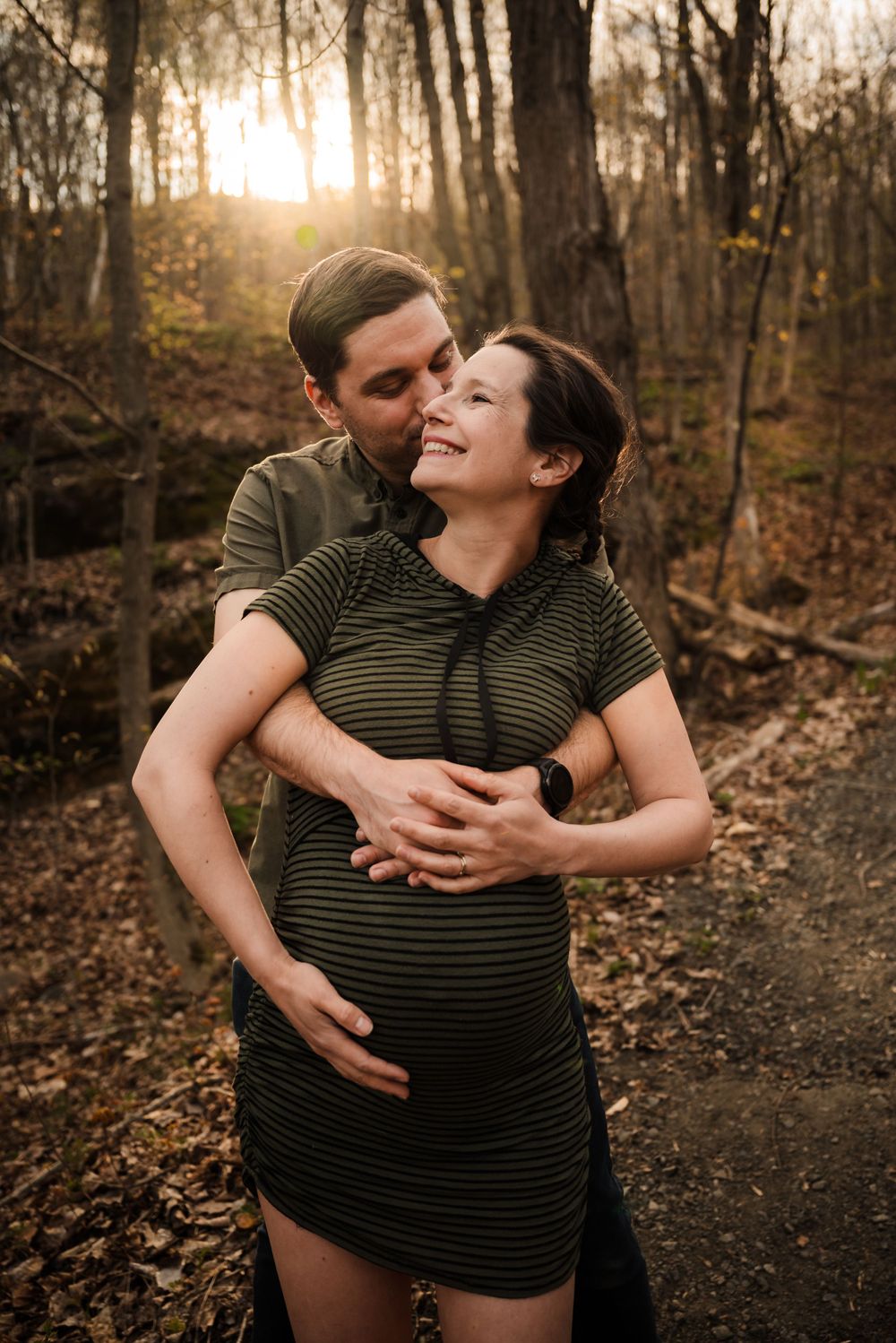 Intimate maternity moment between couple in wooded setting at sunset.