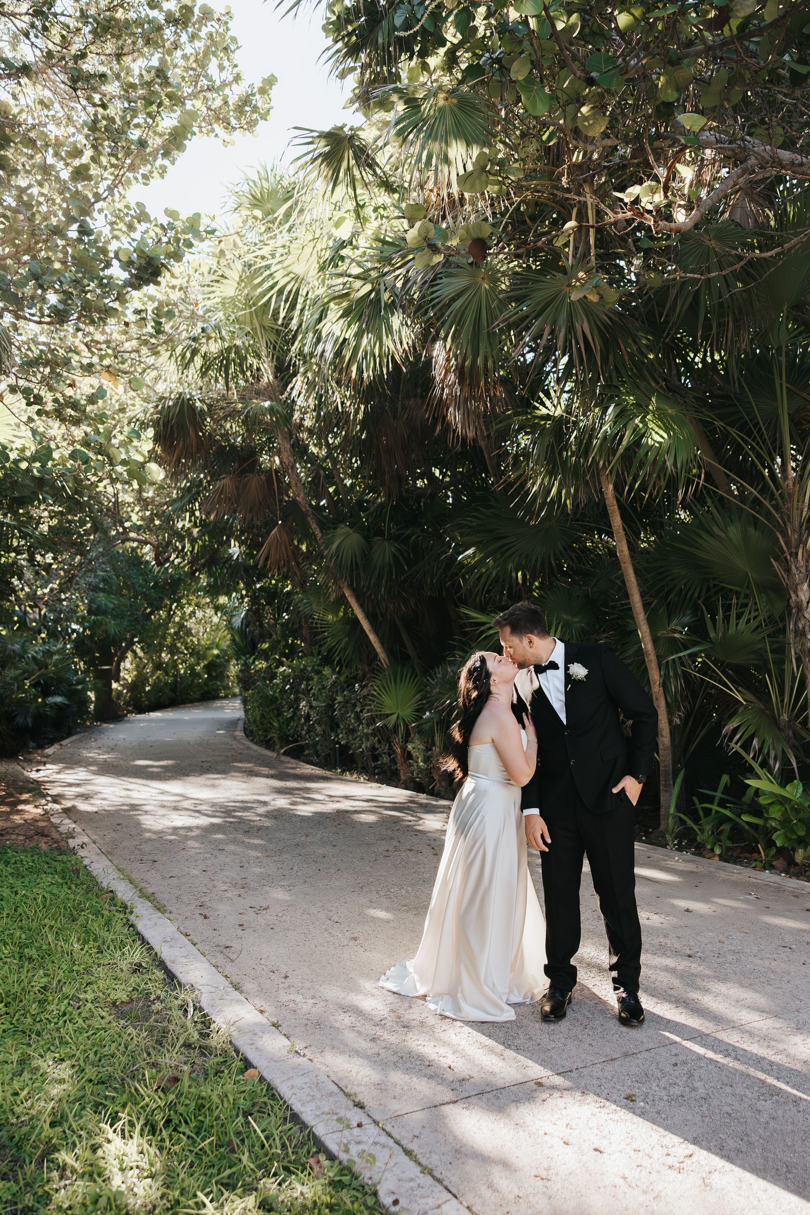 Cancun Mexico Wedding
A couple in wedding attire share an intimate moment on a palm-lined garden pathway.