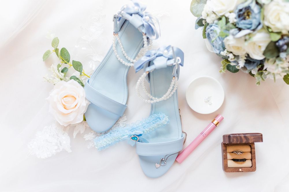 Light blue wedding heels with pearl details styled with pink rose and floral bouquet on white background.