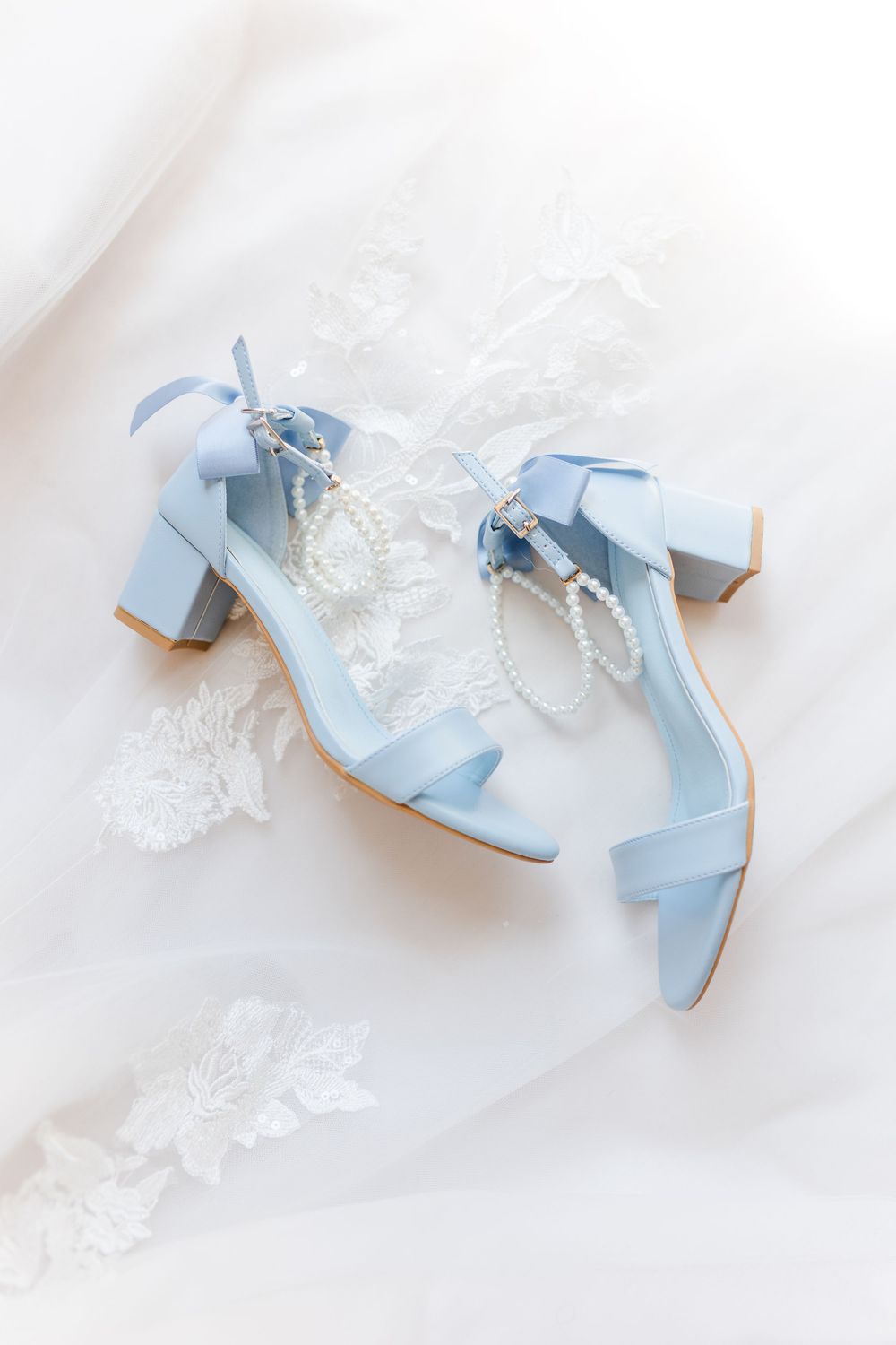 Light blue wedding sandals with block heels displayed on white lace with delicate pearl accessories.