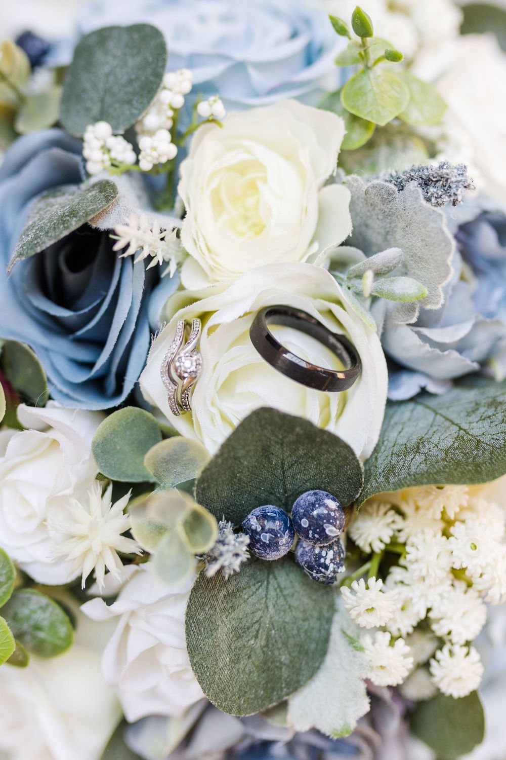 Beautiful wedding bouquet arranged with white roses, dusty blue florals, and eucalyptus leaves with delicate silver accents.