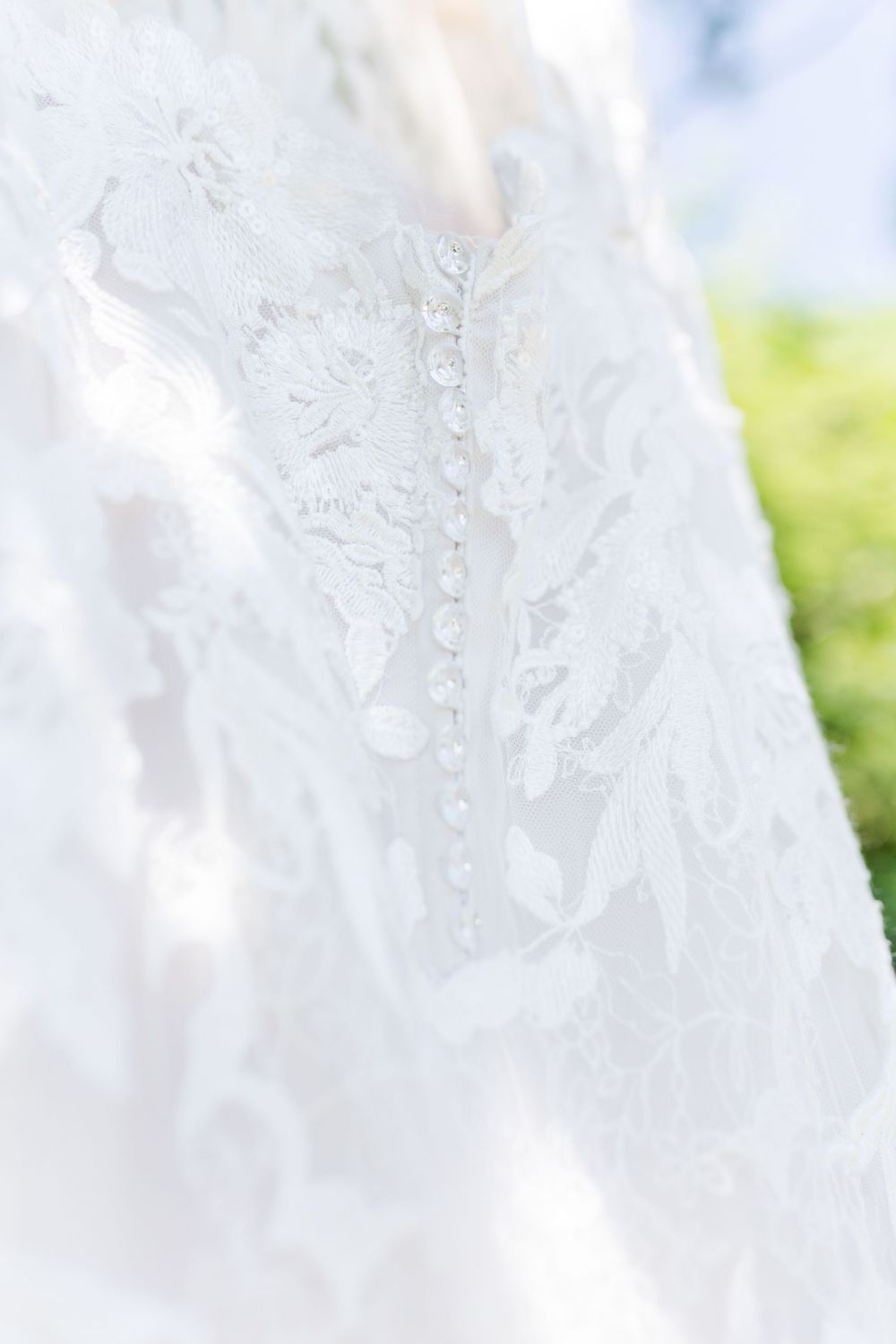 Close-up detail of delicate white lace and beading on a wedding dress against a soft blurred background.