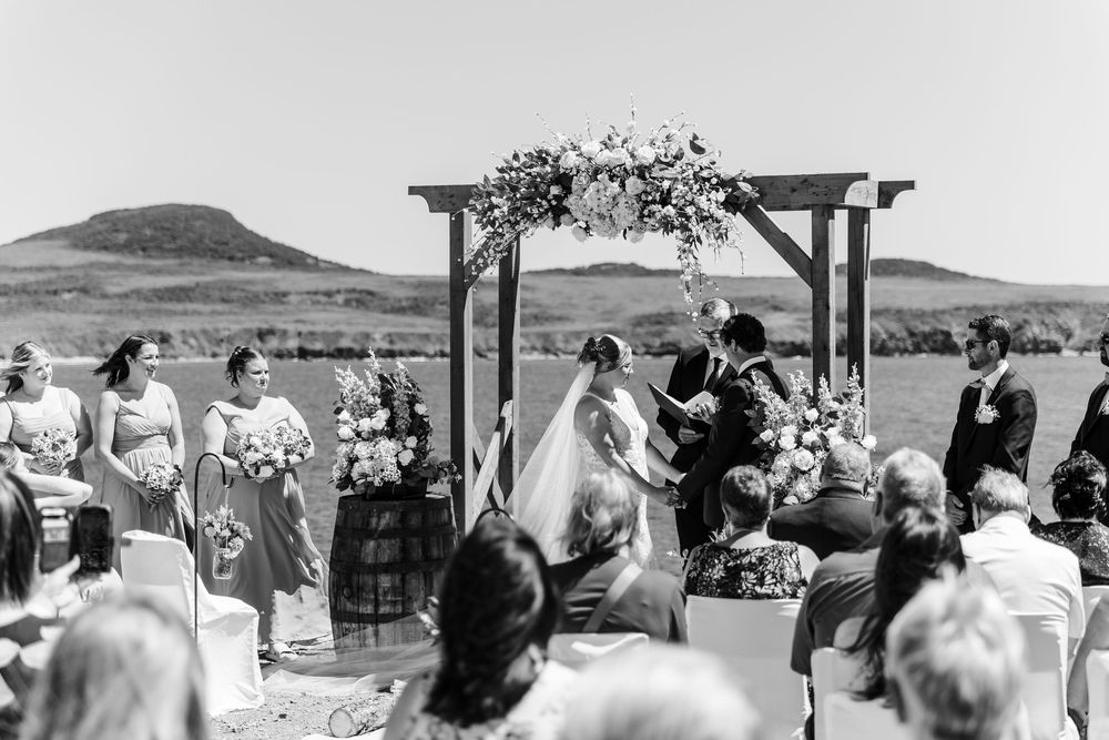 Outdoor wedding ceremony under a floral arch with rolling hills and mountains in the background.