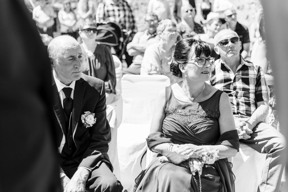 Black and white photo of guests attending an outdoor event wearing formal attire and sunglasses in bright sunlight.