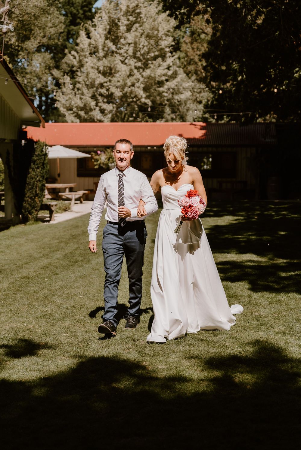 Wedding party runs playfully across a sunny green lawn during outdoor summer celebration.