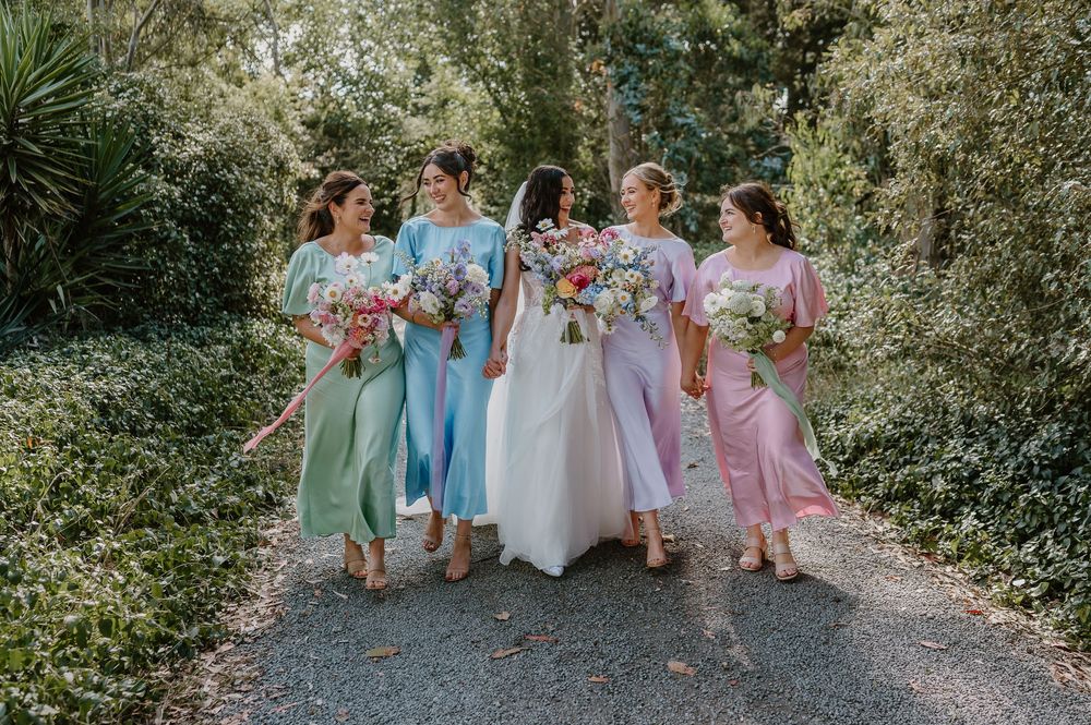 Wedding party dressed in pastel colors poses together on a wooded path during outdoor celebration.