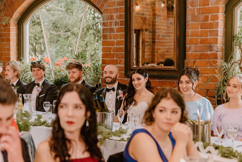 Wedding guests gather for a reception celebration in a rustic brick-walled venue with natural lighting.