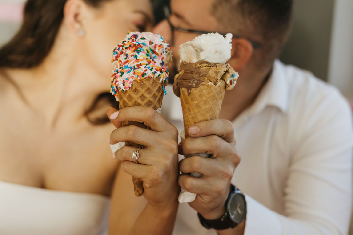A couple holds ice cream cones with sprinkles and whipped cream against a light-colored background at Merla Mae in London Ontario