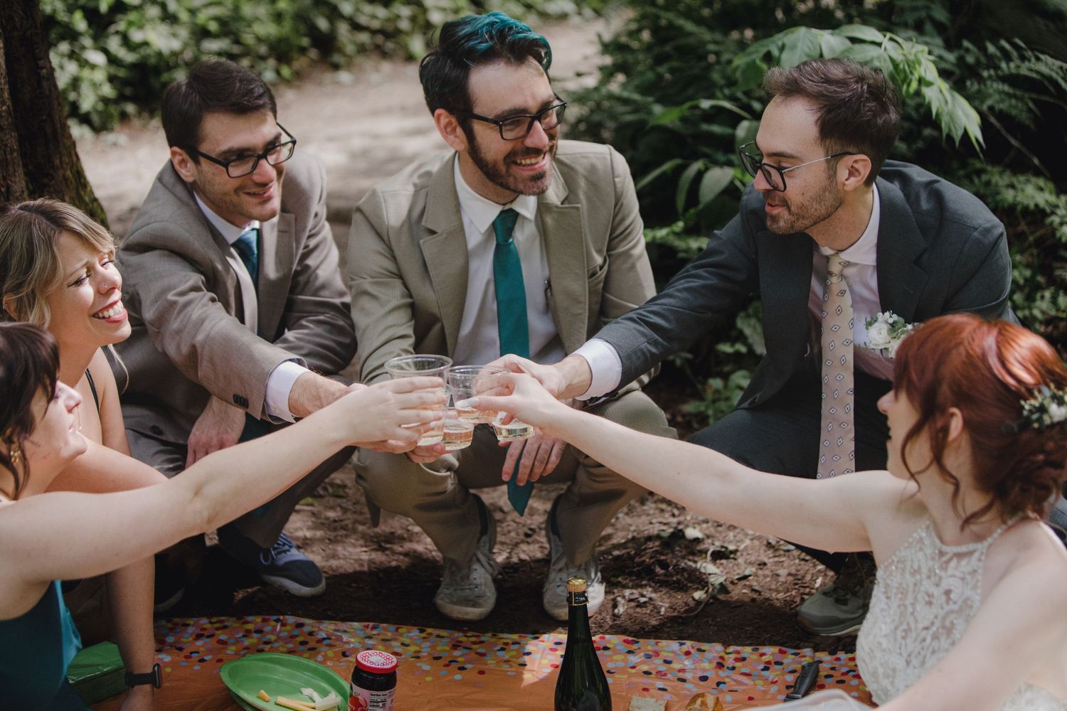 Joyful group toasts and cheers with drinks at an outdoor gathering in a garden setting.
