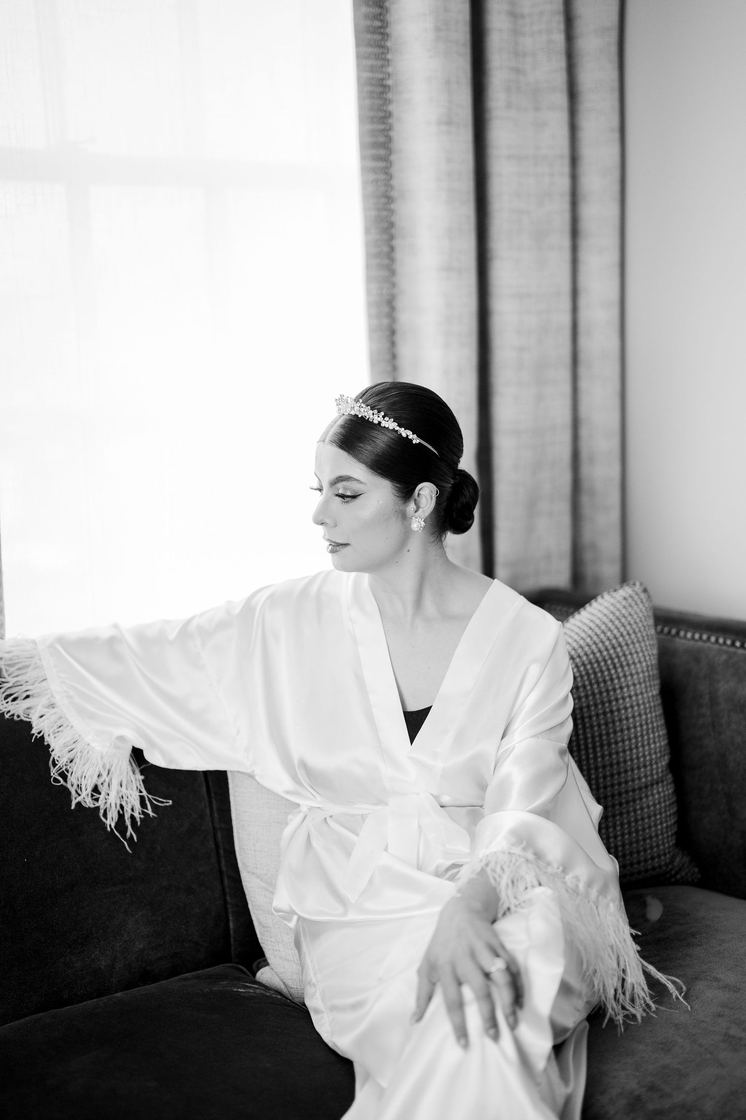 A figure in a white robe sits thoughtfully on a dark couch in black and white photography.