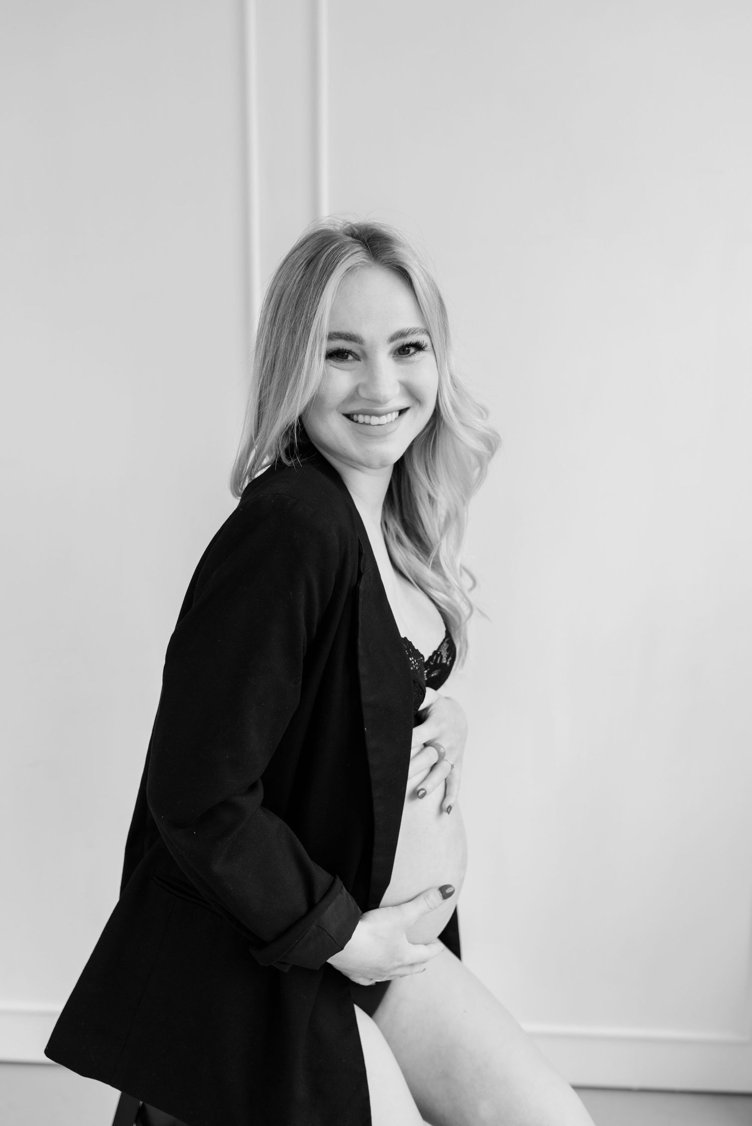 Black and white studio portrait of a woman in a black blazer smiling against a white wall.