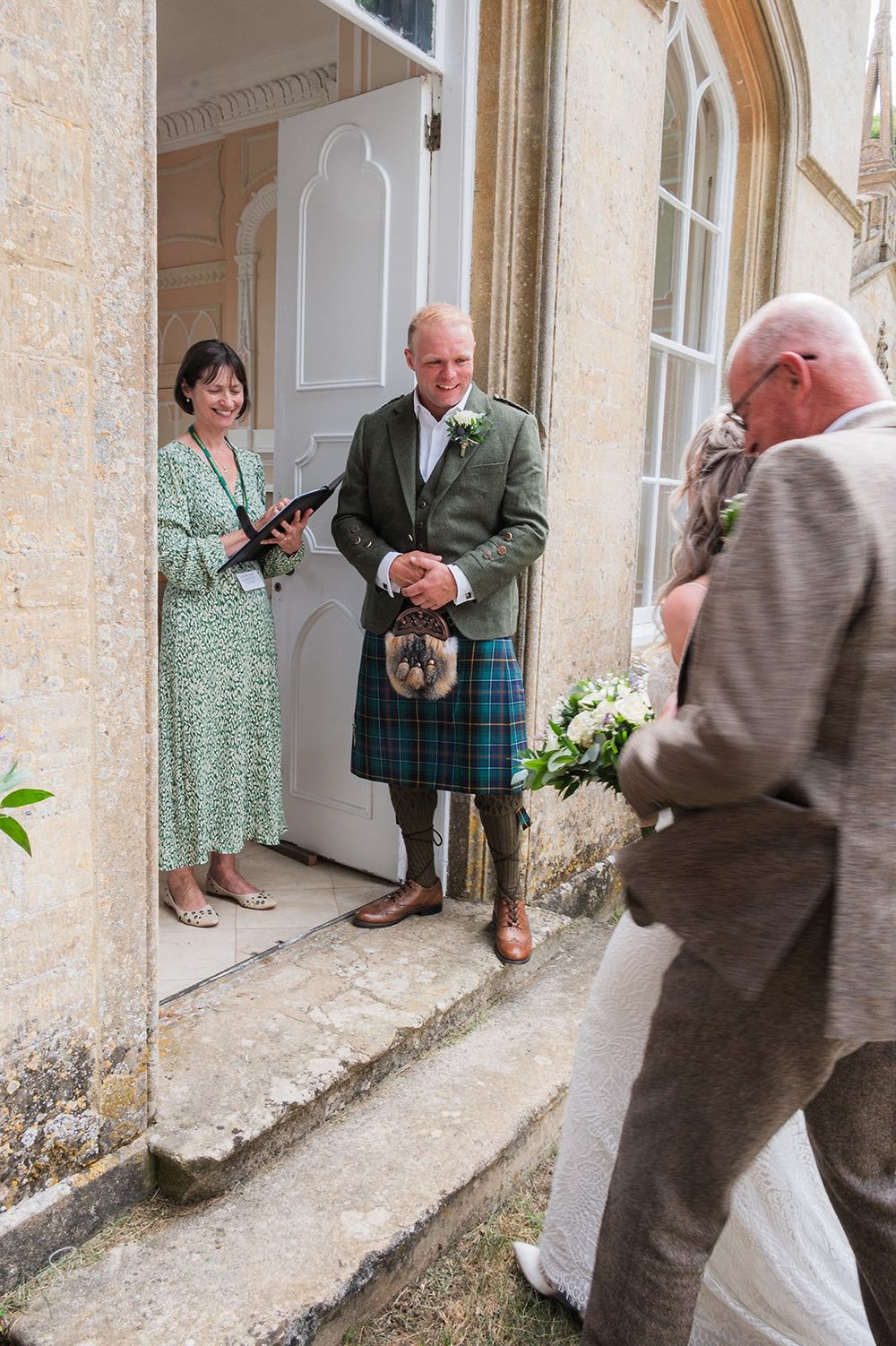 A groom in formal Scottish attire standing outside the traditional stone building entrance to Fort Henry wedding venue.