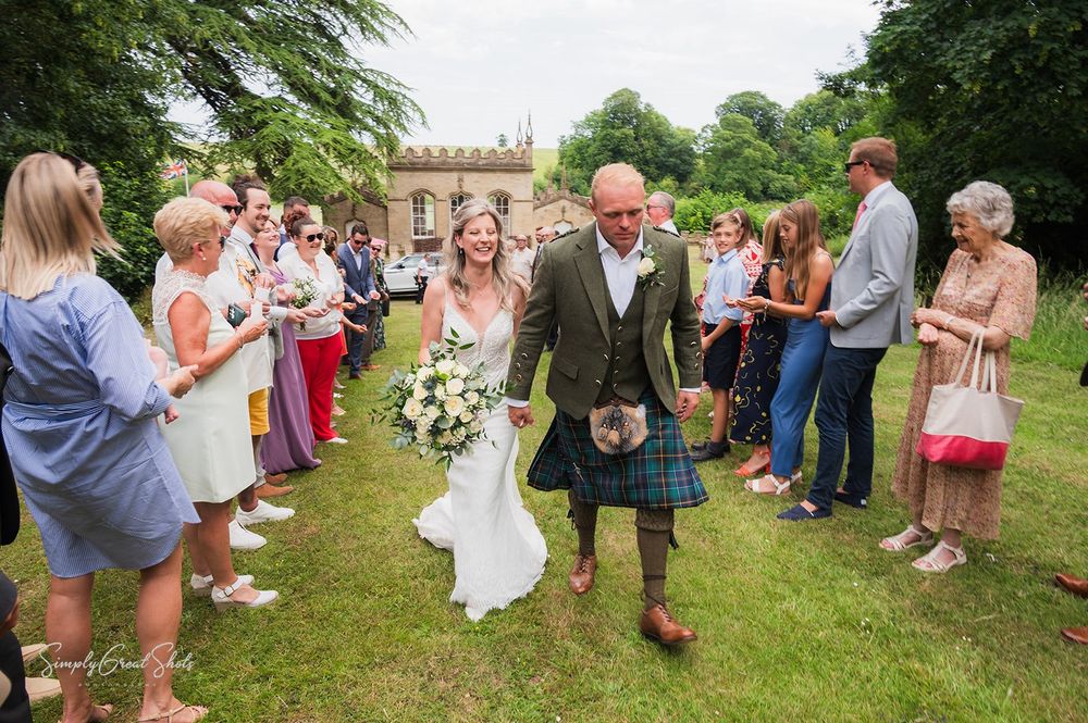 A wedding celebration at Fort Henry's outdoor garden with guests gathered on a green lawn with an ornate archway in background.