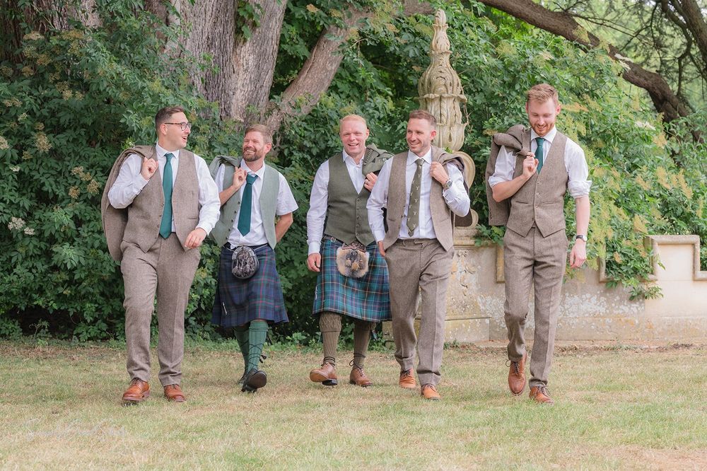 The groom and his groomsmen walk together in a playful pose in the gardens of Fort Henry wedding venue.