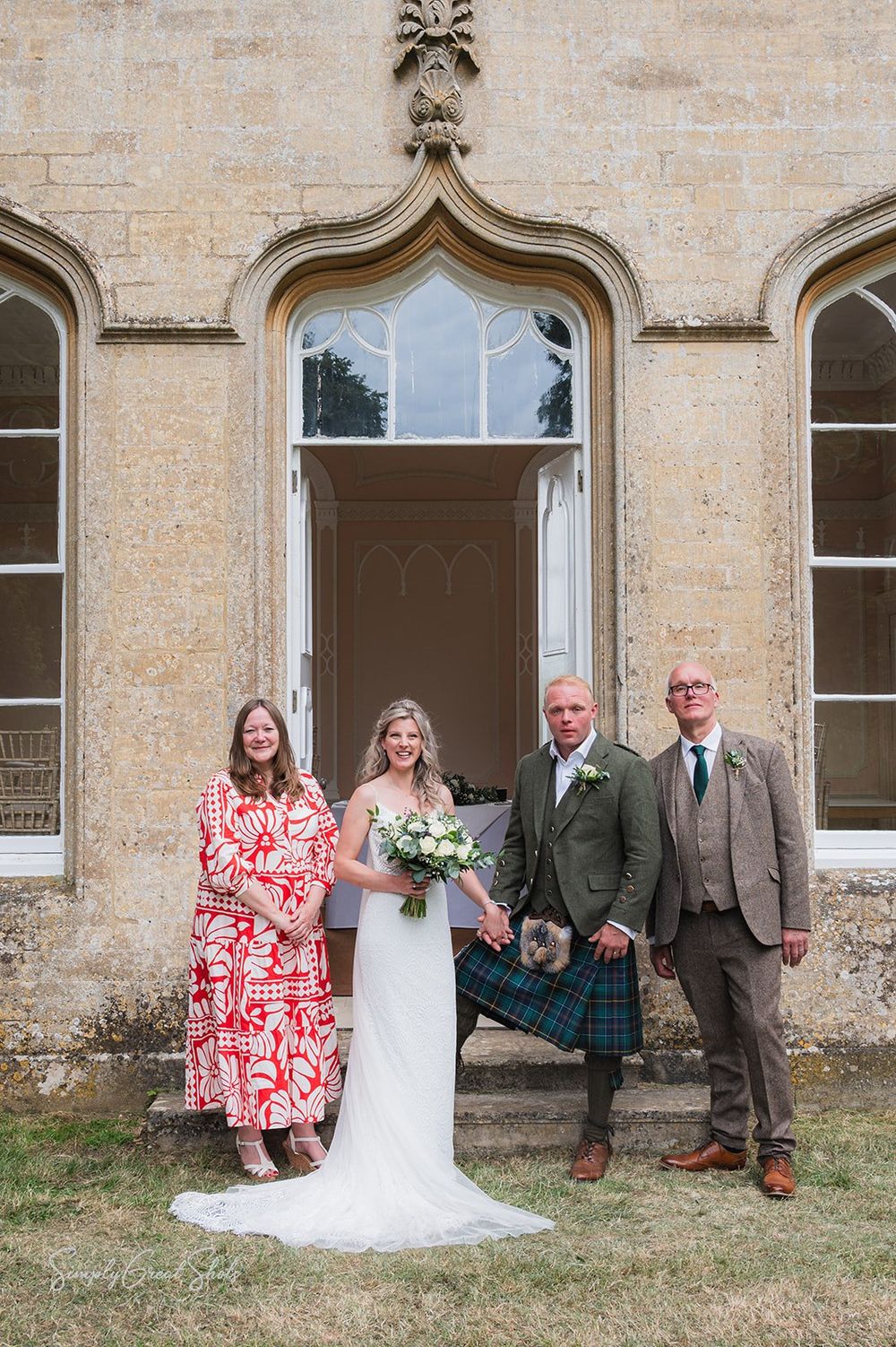 The bride, groom and the groom's parents pose in front of the stone Gothic entrance to Fort Henry, with arched windows.