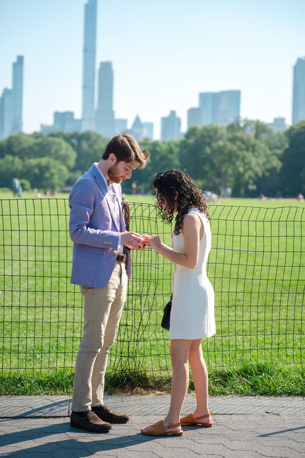 A couple sharing a special moment in front of the New York City skyline at Central Park on a sunny day during a surprise proposal
