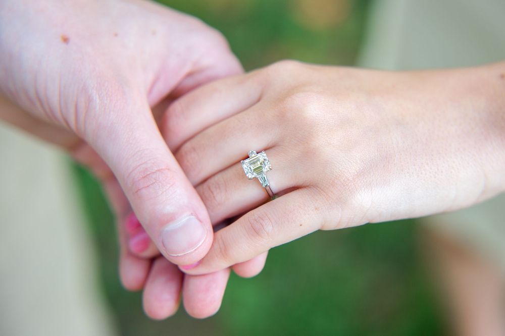 Close-up shot of hands holding each other with a sparkling diamond engagement ring displayed on one hand.