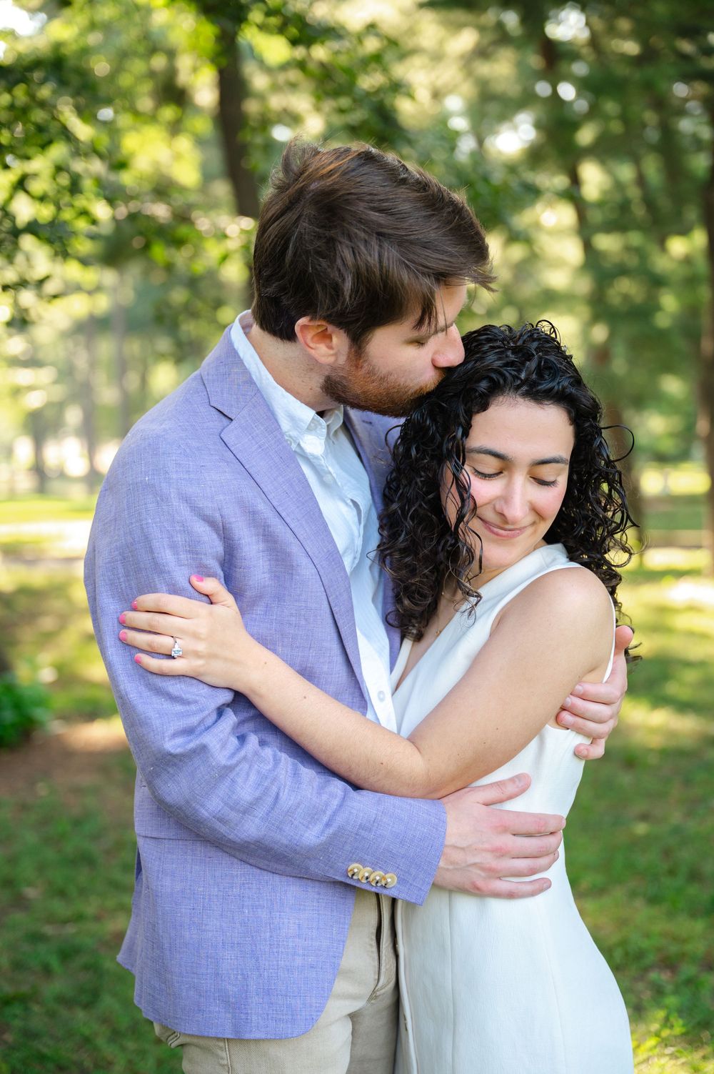Couple shares tender embraces in a sunlit garden setting with lush green trees in the background in Central Park.