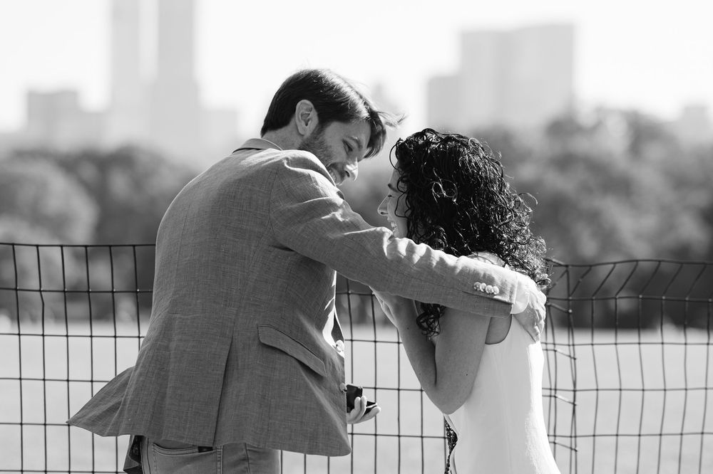 A black and white photo of a man hugging his new fiancée during a surprise proposal in NYC. Photo by Joliette Marie Photography.