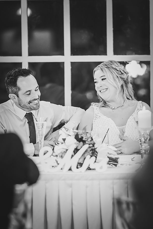 A candid black and white reception moment of newlyweds sharing laughter at their head table.