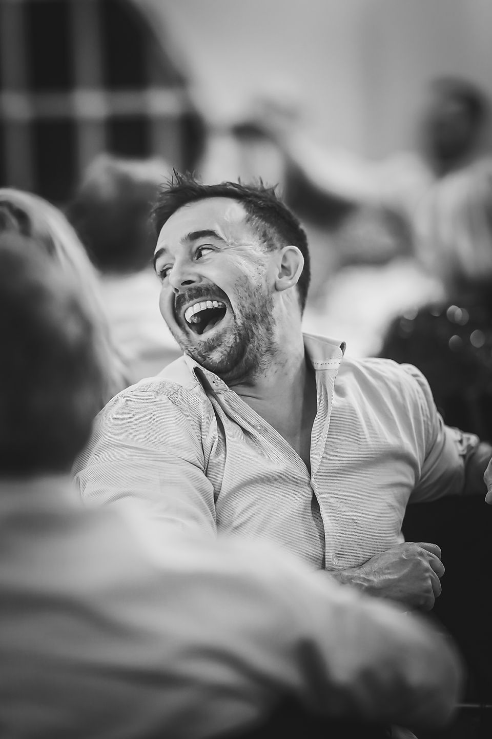 Black and white candid photograph of a person laughing joyfully while wearing a light colored button-down shirt.