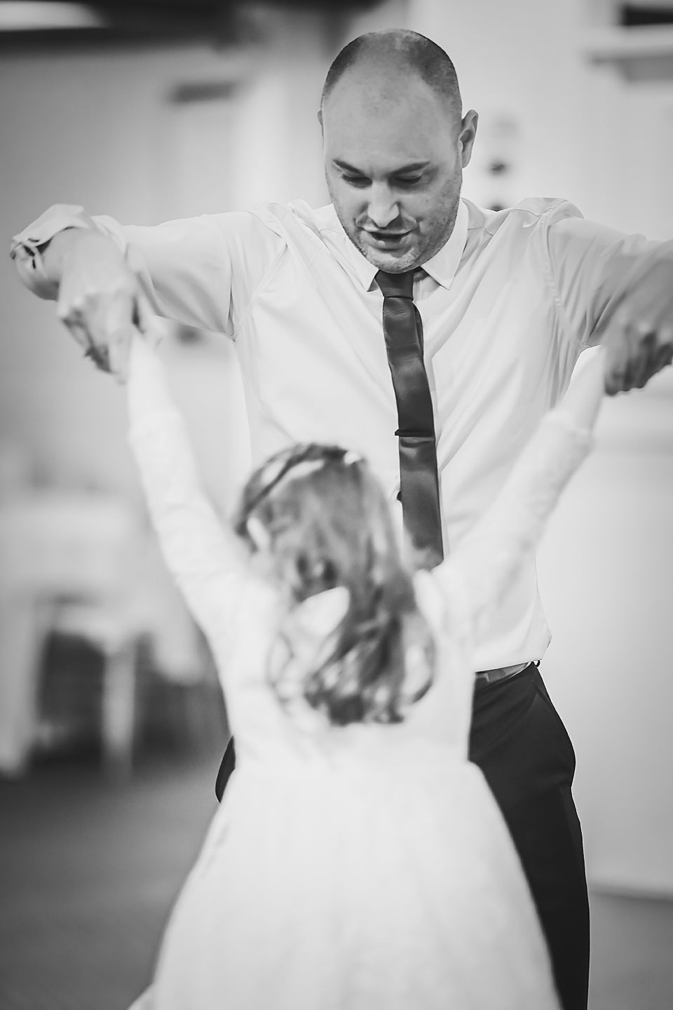 Black and white photo capturing a joyful father-daughter dance at a wedding reception.