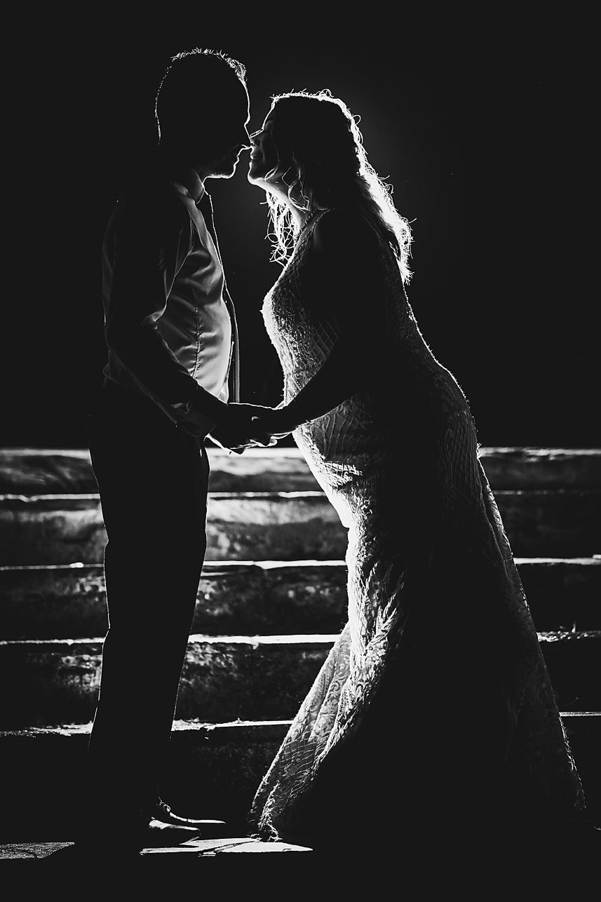 Dramatic silhouette of newlyweds in intimate pose against backlit stairs in black and white.