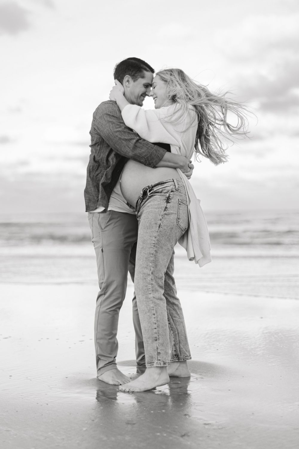 Black and white beach photo of couple dancing in waves.