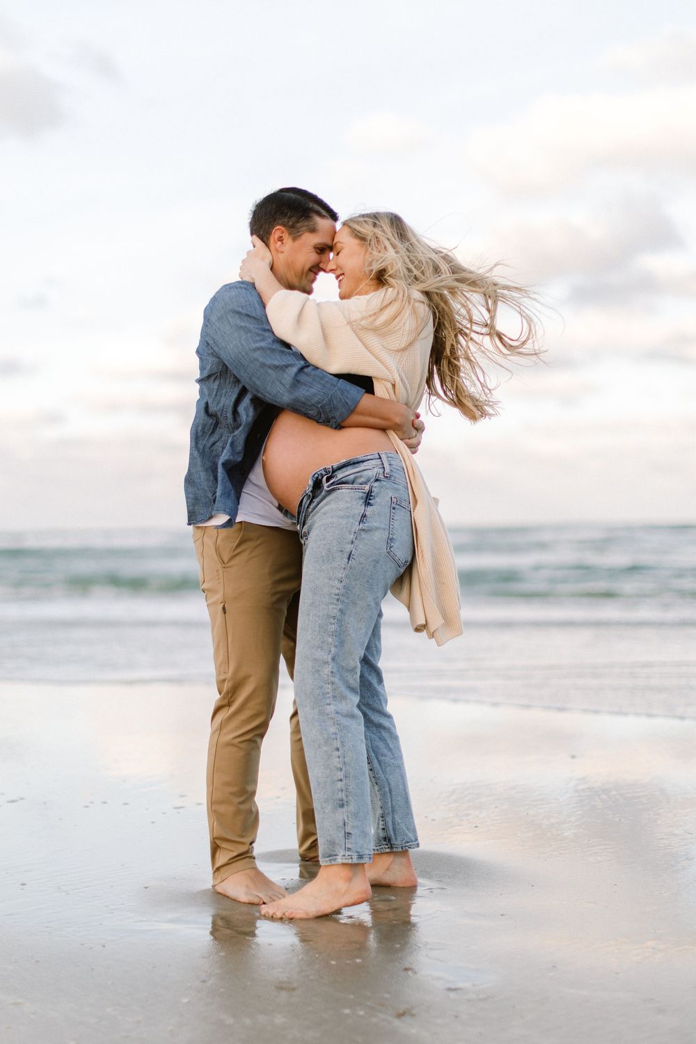 A romantic embrace between a couple on a sandy beach with the ocean behind them.