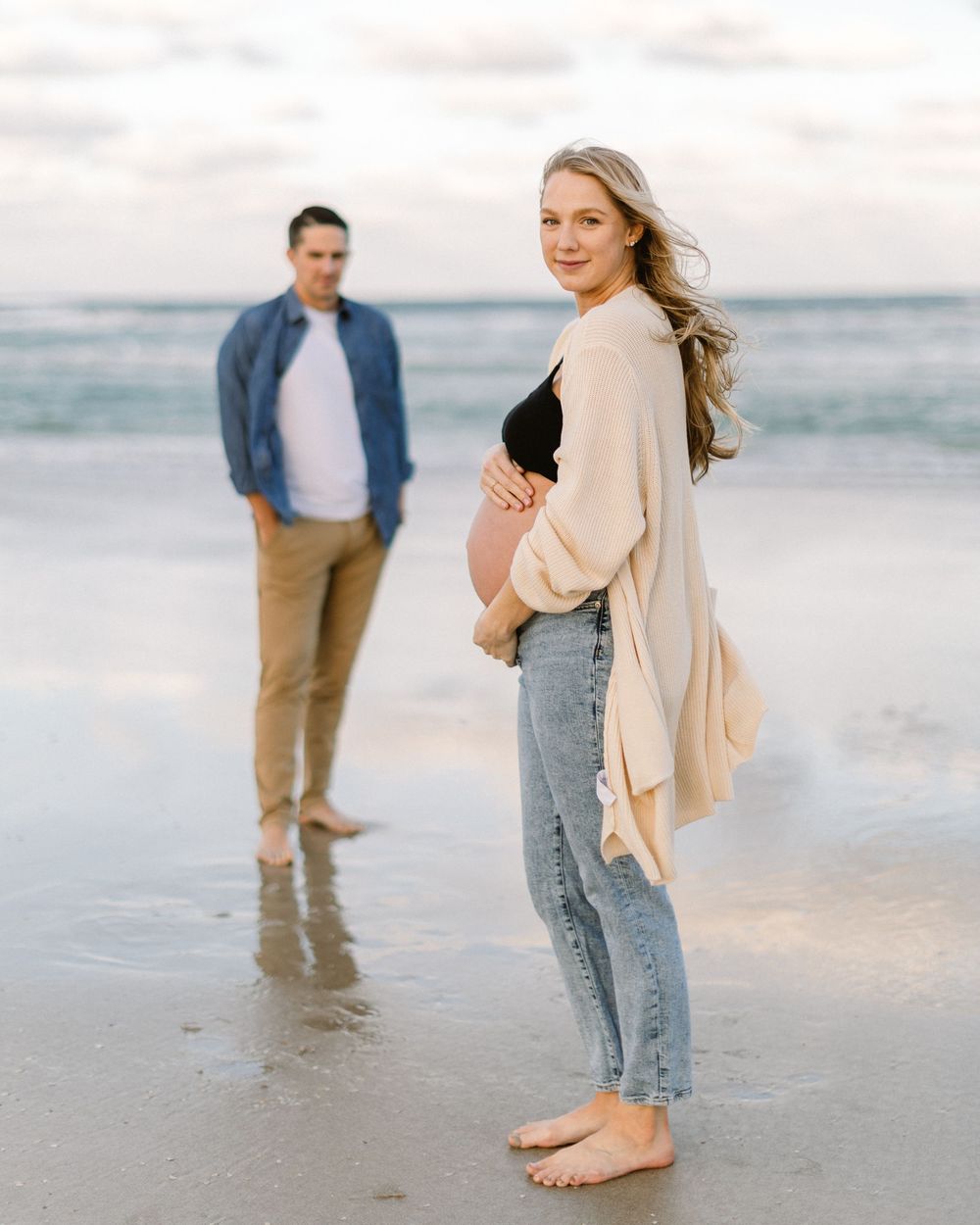 A couple shares an intimate moment on a beach at sunset with ocean waves in the background.