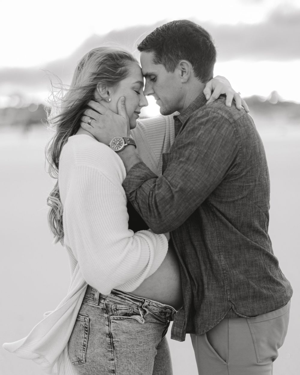 An intimate black and white portrait of a couple embracing on a beach.