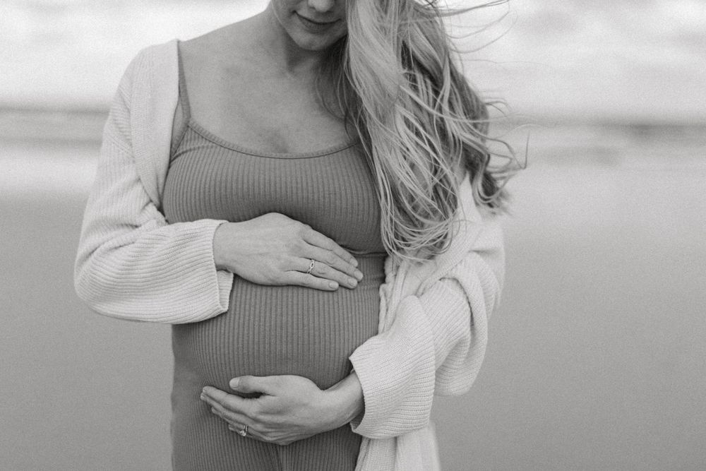 A black and white portrait of an expectant mother tenderly holding her baby bump.