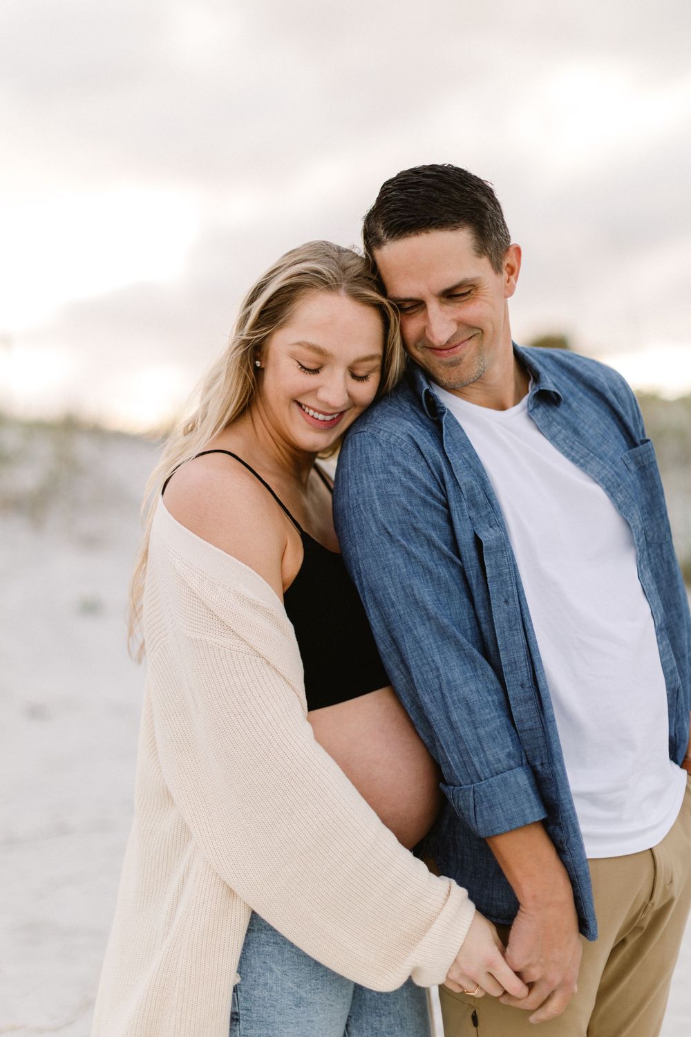 A couple shares a gentle moment of connection on a sandy beach.