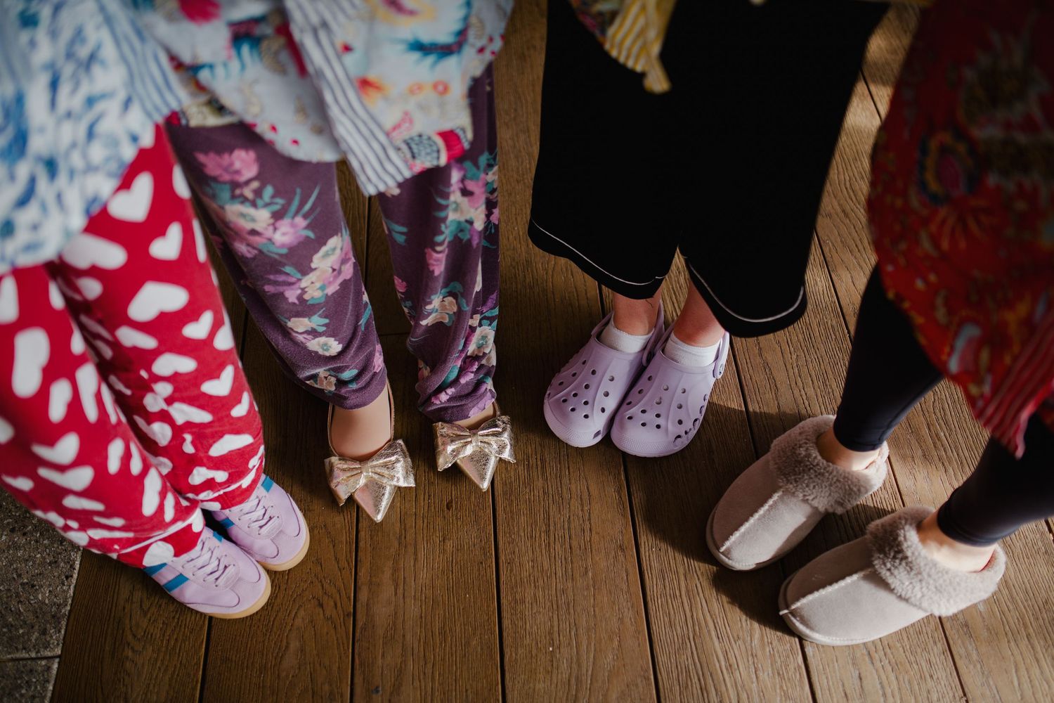 Several pairs of legs wearing colorful socks and comfortable shoes stand together on a wooden floor.