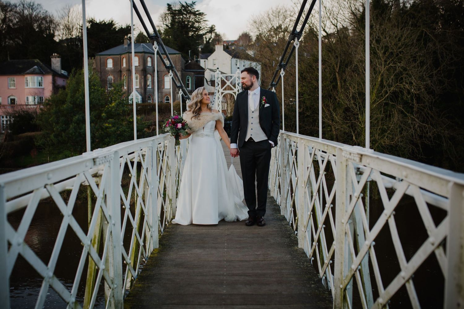 A couple stands together on a white pedestrian bridge during their wedding photoshoot.