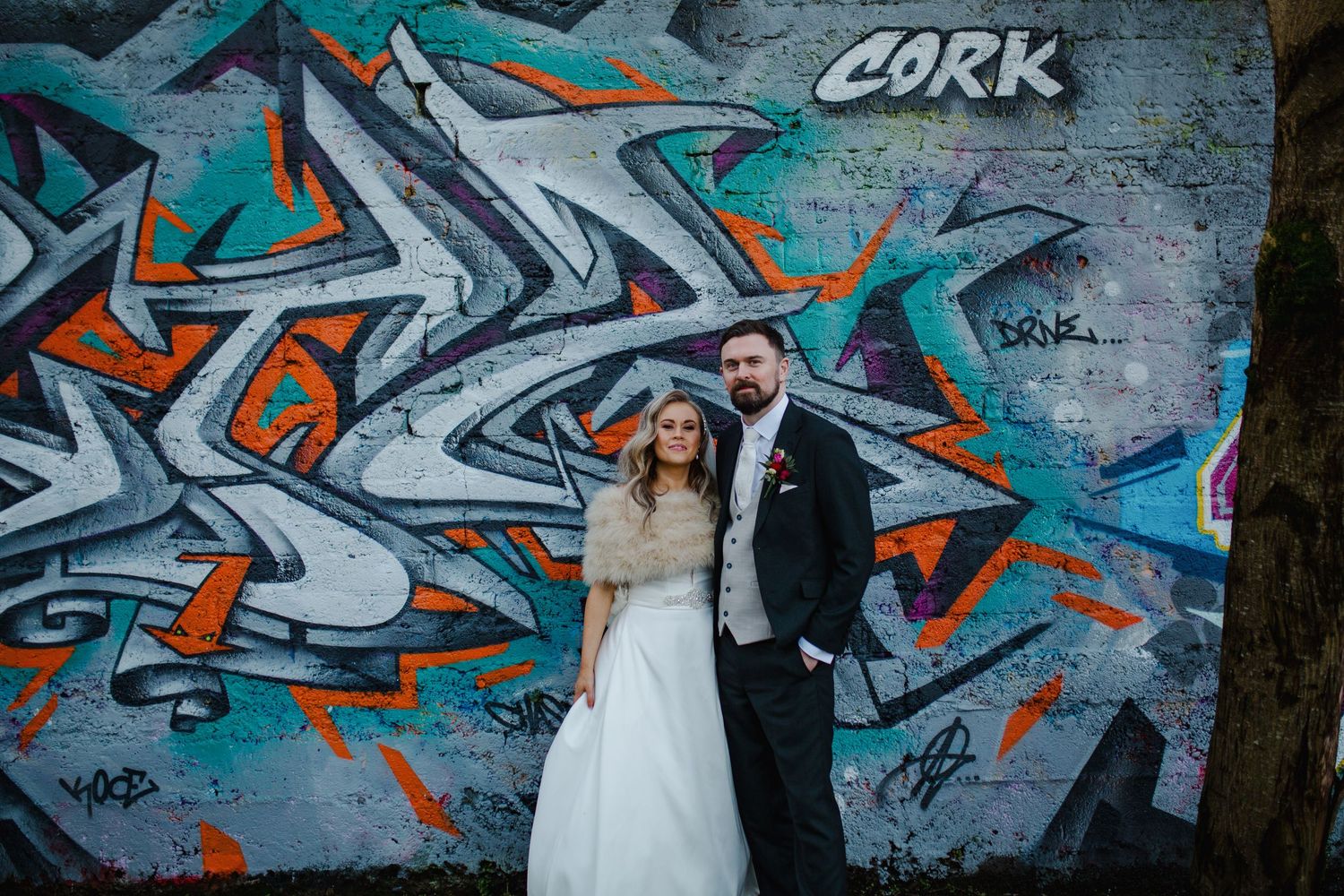 Wedding couple poses together against a vibrant graffiti wall featuring teal and orange street art designs.