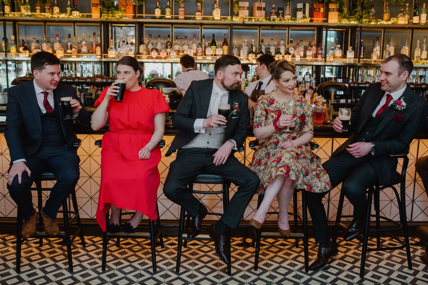 Group of wedding guests sitting at tables and mingling in an elegant venue with ornate checkered flooring and bar decor.