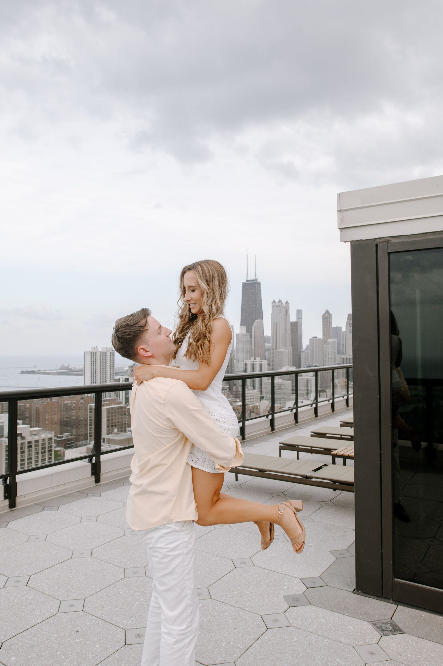 A romantic couple embraces on a rooftop terrace with the Chicago skyline visible in the background.