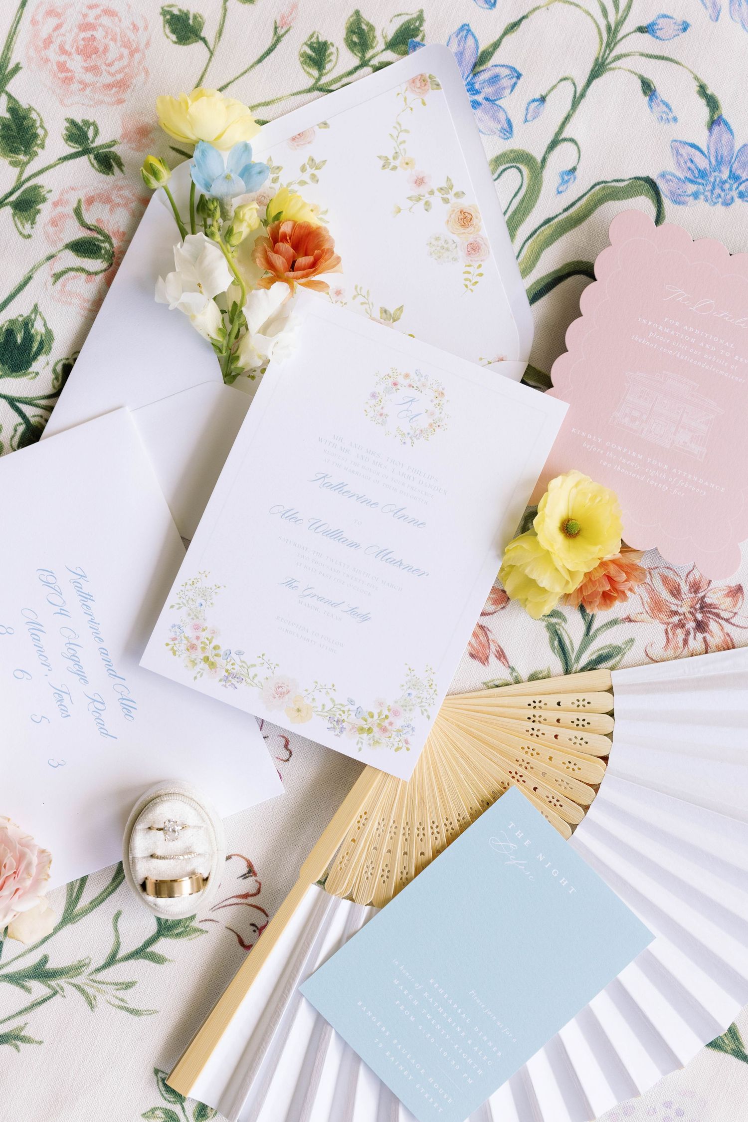 Wedding stationery styled with floral elements, decorative fan, and fresh blooms in pastel pink, blue and yellow tones.