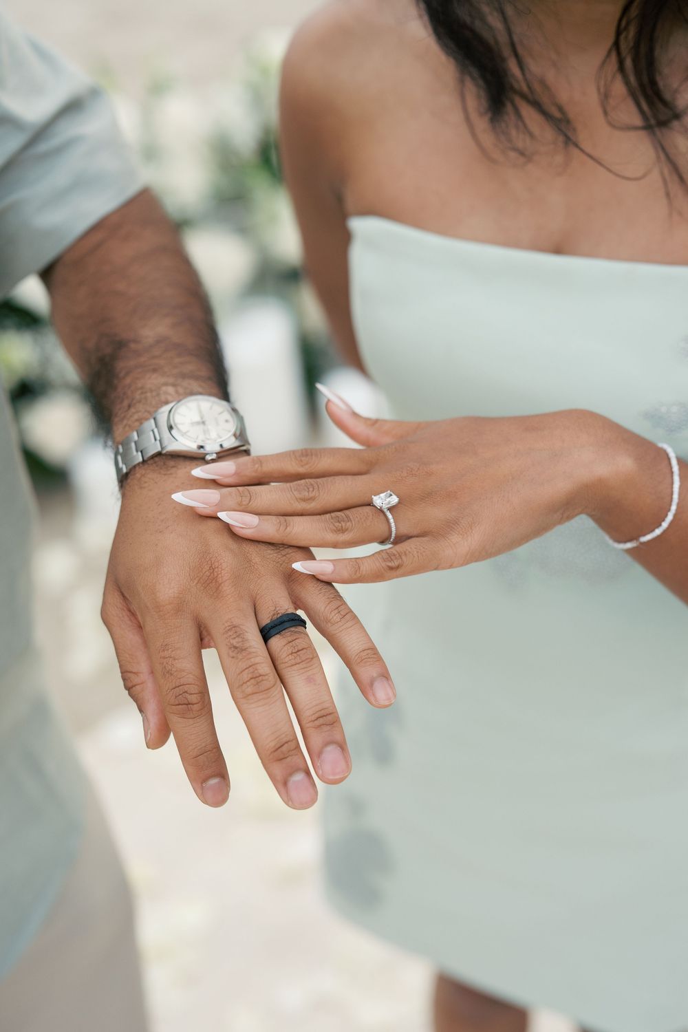 Close-up of hands displaying an engagement ring with a sparkling diamond solitaire on white background.