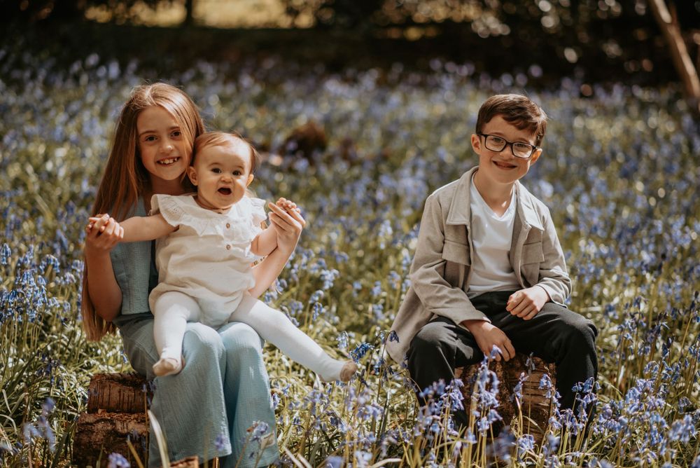 Children sit in a meadow of blue wildflowers on a sunny afternoon.