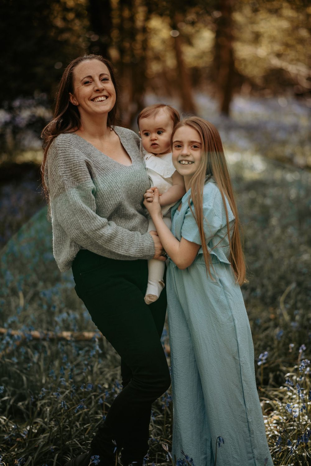 A family poses together outdoors in the woods wearing casual clothing on an autumn afternoon.