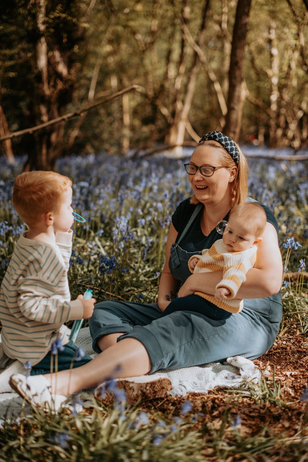 Family enjoying a spring afternoon together sitting among blooming bluebells in a wooded forest setting.
