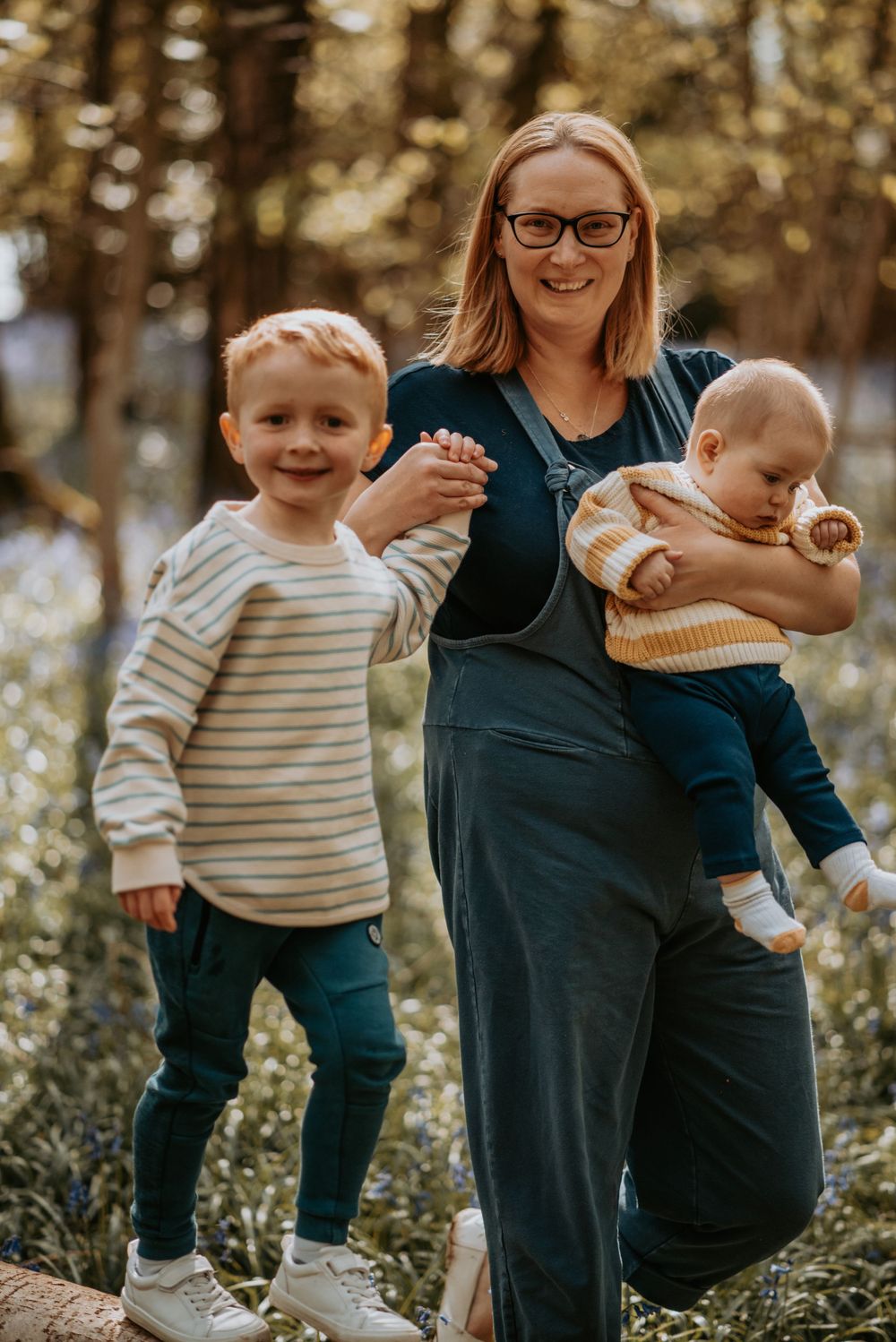A family poses together outdoors in a wooded setting wearing casual clothing on an autumn day.