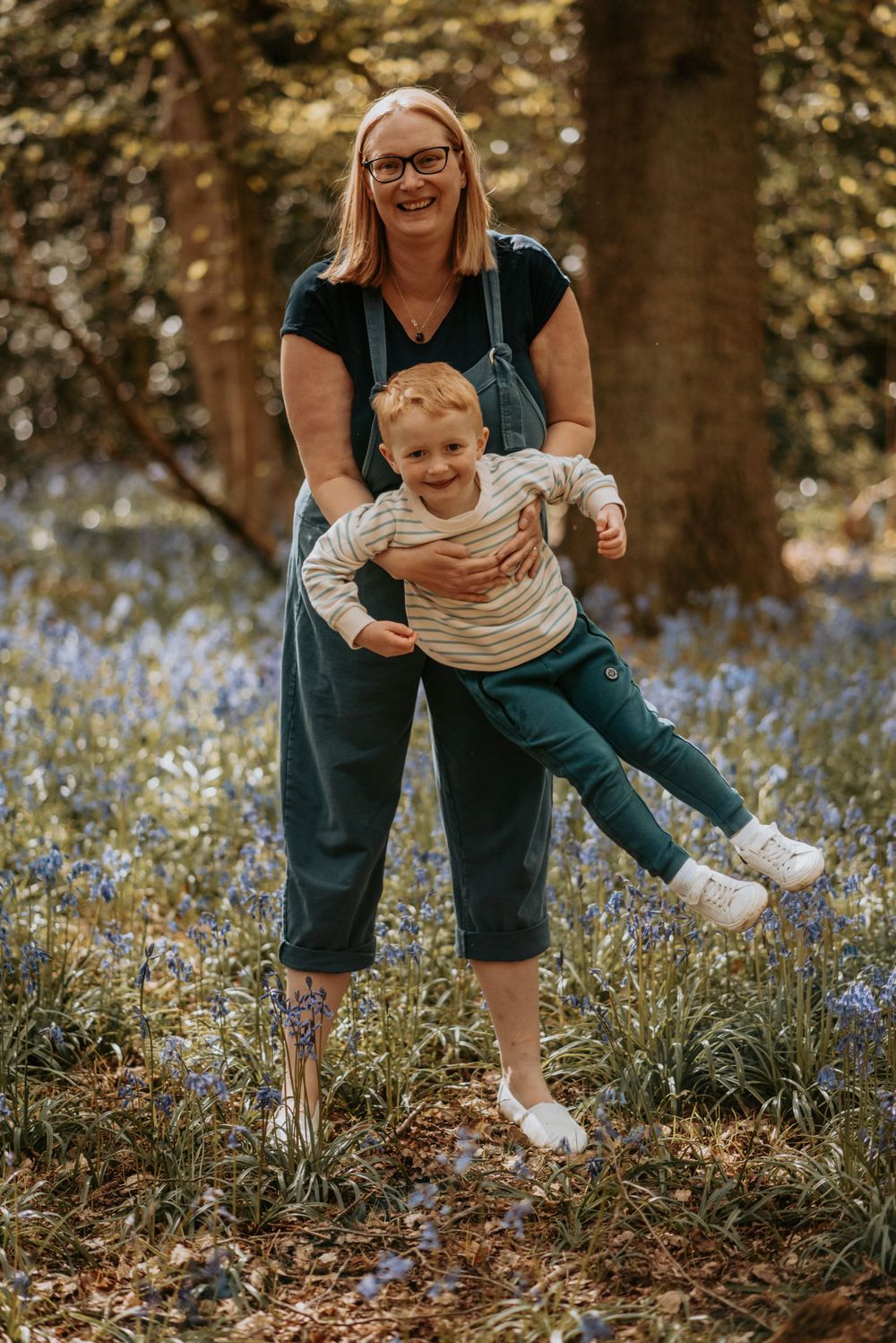 Playful moment captured in a forest of bluebells as a parent and child share laughter and joy on an autumn day.