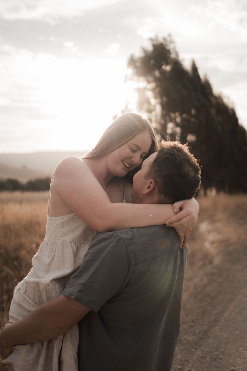 A romantic sunset moment captured as a couple embraces on a dirt path in a golden field at dusk.