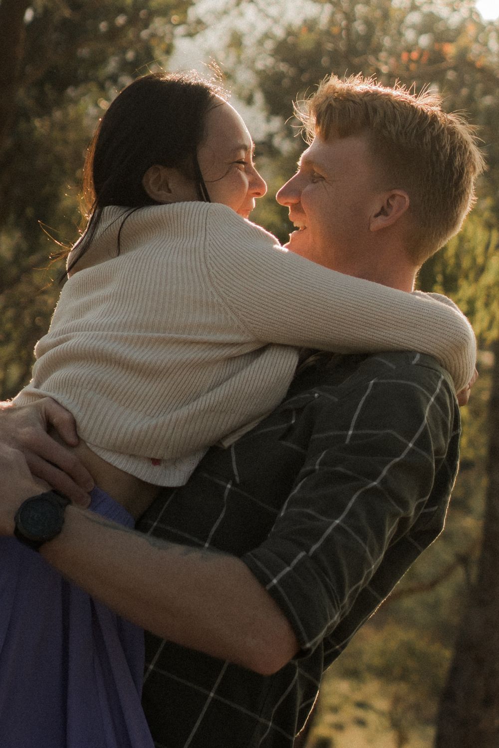 A couple embraces intimately in warm golden sunlight during sunset outdoors.