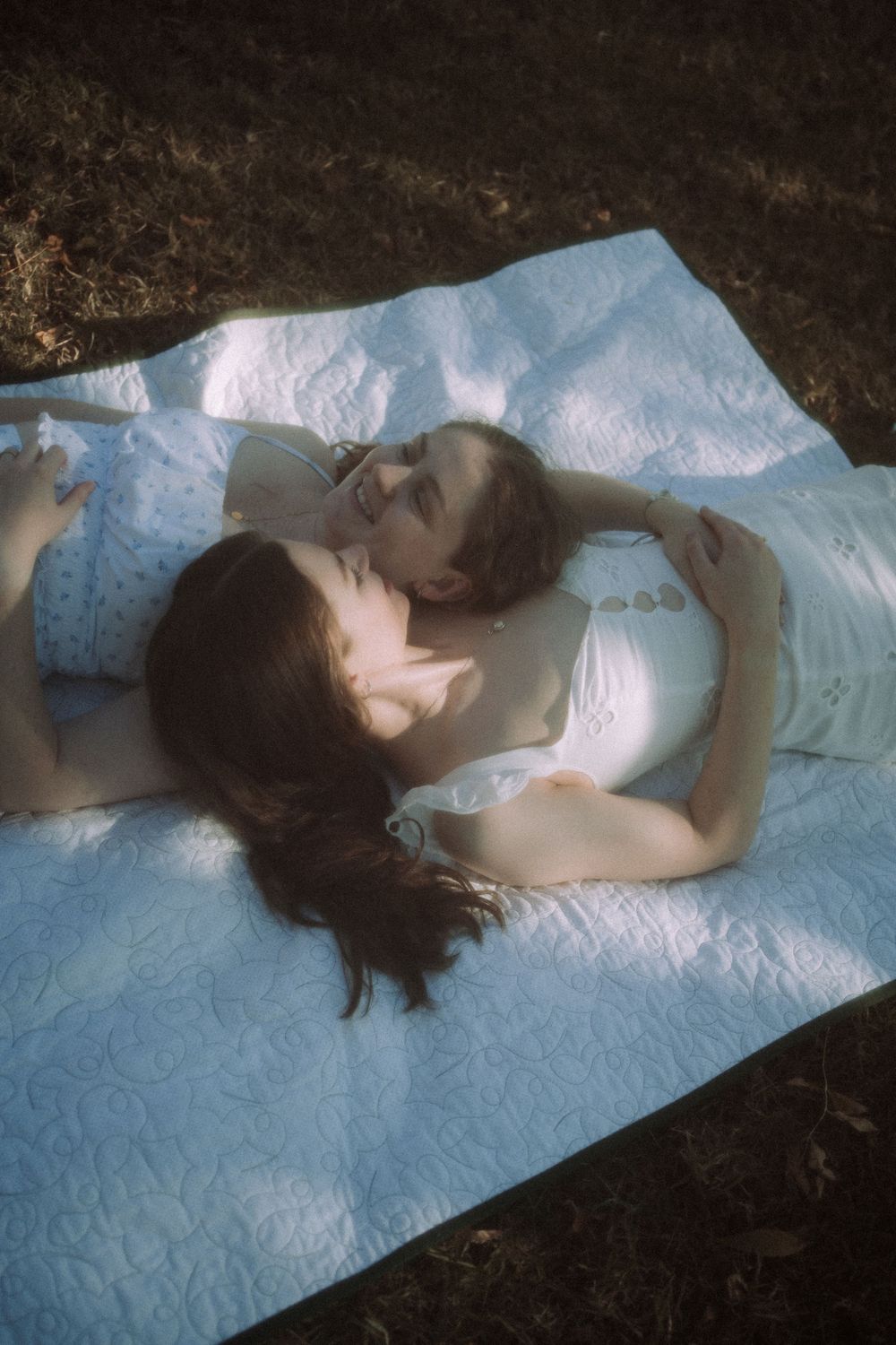 Two people lie peacefully on a light blue blanket in soft, dreamy lighting.