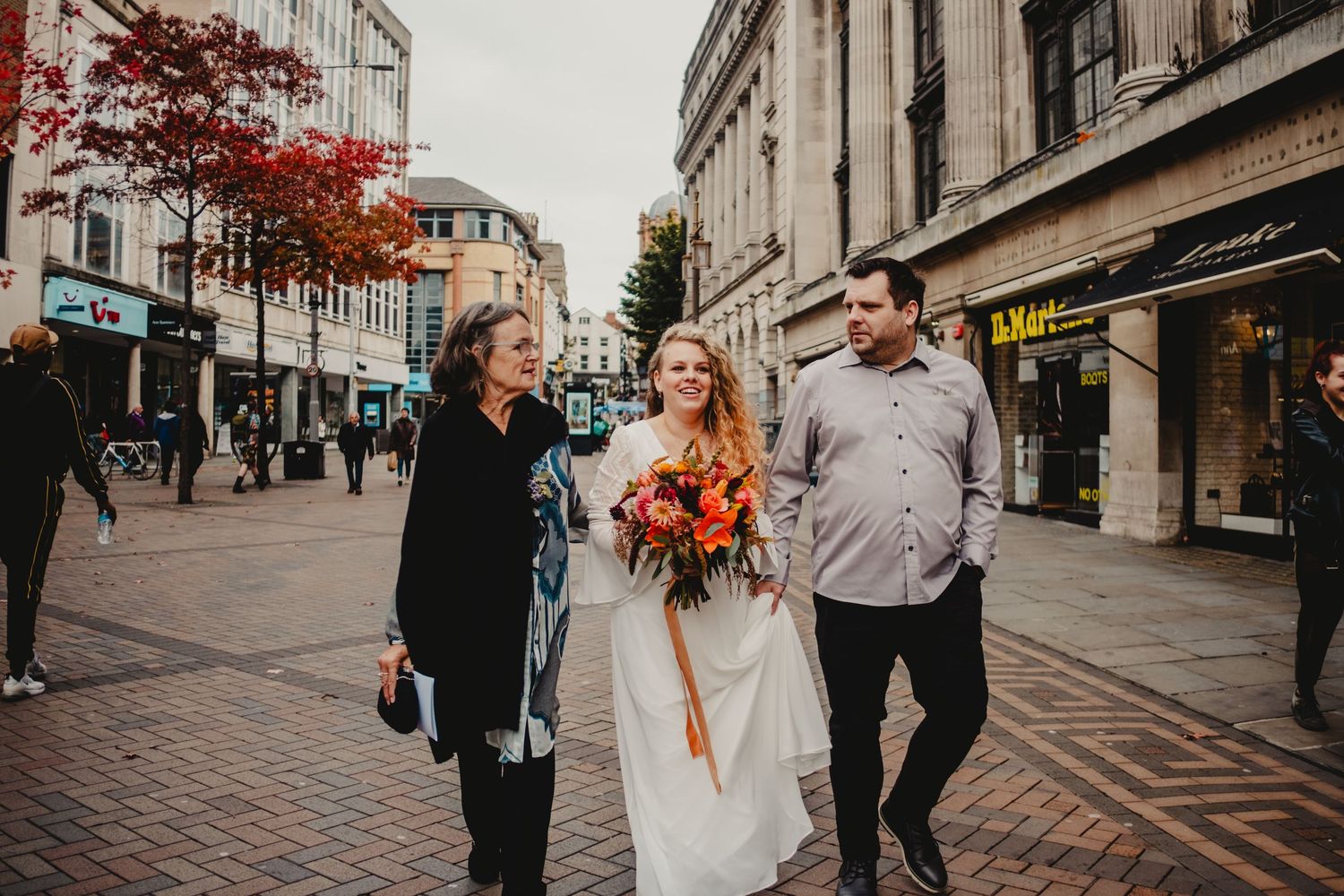 Three people walk down a charming brick-paved city street with autumn trees and historic buildings in Nottingham, England